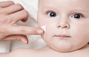 Vuxen persons hand som applicerar kräm i ansiktet på en baby.