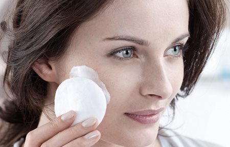 Kvinna som applicerar kräm i ansiktet med en bomullsrondell