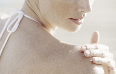 Kvinna som applicerar kräm på sin högra axel.